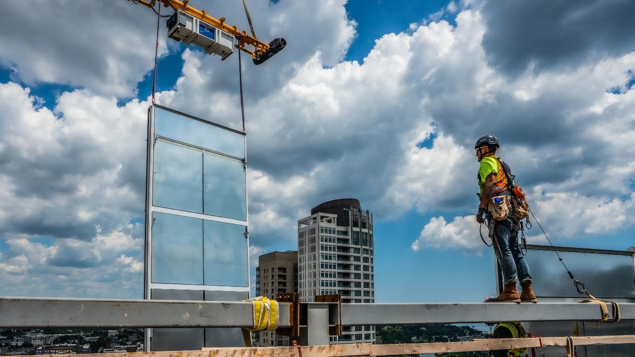 A construction crew member guides one of the glass panels into place on the North Building. Credit: Kenny Yoo Photography