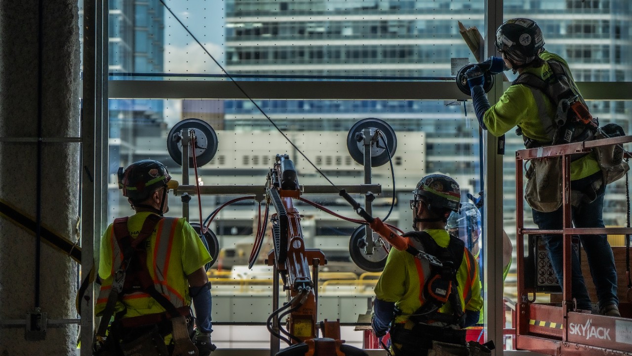 Construction team members position one of the final glass panels on the North Building. Photo credit: Kenny Yoo