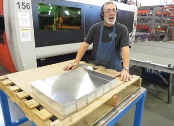 Mark Derderian stacks reflector parts next to a laser machine that is cutting them out.