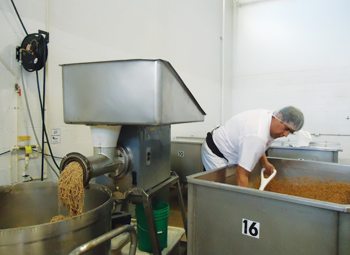 Hector Rivera shovels sprouted grains into a grinder to be readied for bread dough.